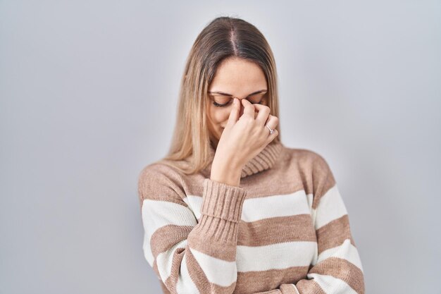 Giovane donna bionda che indossa un maglione a collo alto su sfondo isolato stanco sfregamento naso e occhi sensazione di affaticamento e mal di testa stress e concetto di frustrazione