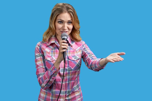 Giovane donna bionda che indossa una camicia a scacchi in piedi con un microfono isolato su sfondo blu