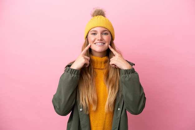 Giovane donna bionda che indossa una giacca invernale isolata su sfondo rosa sorridente con un'espressione felice e piacevole