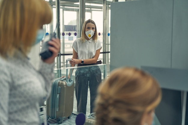 Giovane donna bionda che indossa una maschera protettiva mentre guarda i lavoratori dell'aeroporto