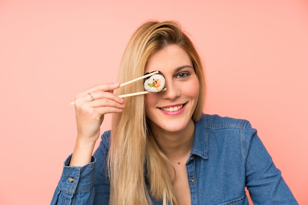 Giovane donna bionda che mangia i sushi sopra la parete dentellare