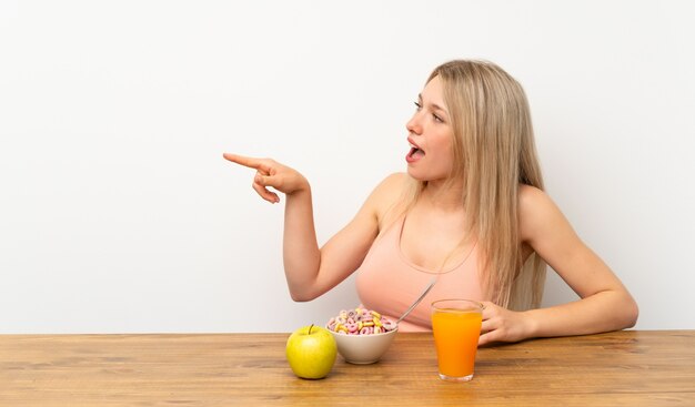 Giovane donna bionda che mangia prima colazione che indica dito il lato