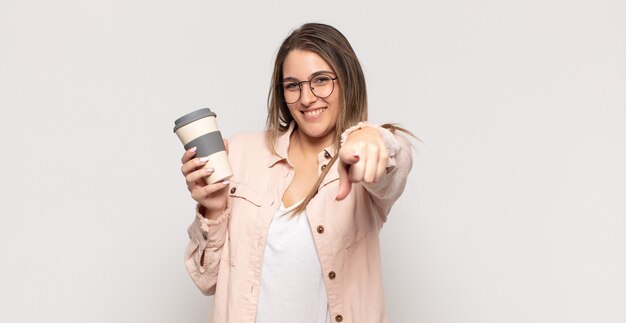 Giovane donna bionda che punta davanti con un sorriso soddisfatto, fiducioso, amichevole, scegliendo te