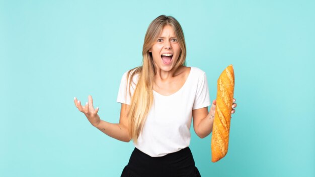 Giovane donna bionda che sembra arrabbiata, infastidita e frustrata e con in mano una baguette di pane