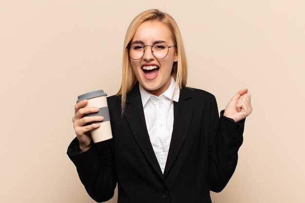 Giovane donna bionda che sembra estremamente felice e sorpresa, celebrando il successo, gridando e saltando