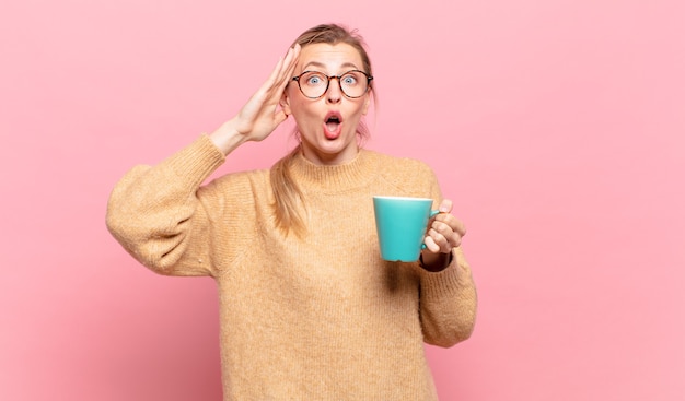 Giovane donna bionda che sembra felice, stupita e sorpresa, sorride e realizza una buona notizia incredibile e incredibile. concetto di caffè