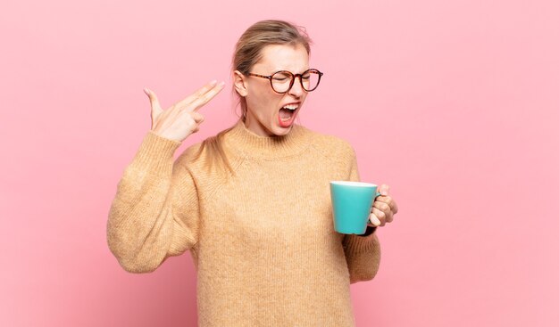 Giovane donna bionda che sembra infelice e stressata, gesto suicida che fa il segno della pistola con la mano, indicando la testa. concetto di caffè