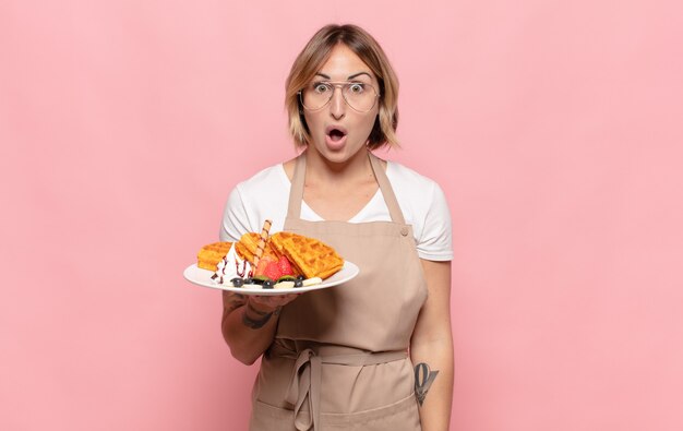 Giovane donna bionda che sembra molto scioccata o sorpresa, fissando con la bocca aperta dicendo wow