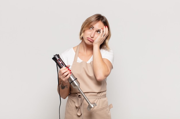 Giovane donna bionda che si sente annoiata, frustrata e assonnata dopo un compito noioso, noioso e noioso, tenendo la faccia con la mano