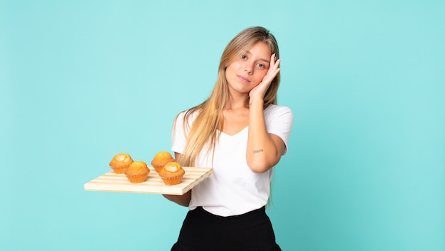 Giovane donna bionda che si sente annoiata, frustrata e assonnata dopo una noiosa e con in mano un muffin troy