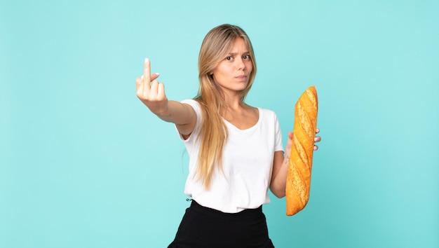 Giovane donna bionda che si sente arrabbiata, infastidita, ribelle e aggressiva e tiene in mano una baguette di pane