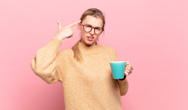 Giovane donna bionda che si sente confusa e perplessa, mostrando che sei pazzo, pazzo o fuori di testa. concetto di caffè