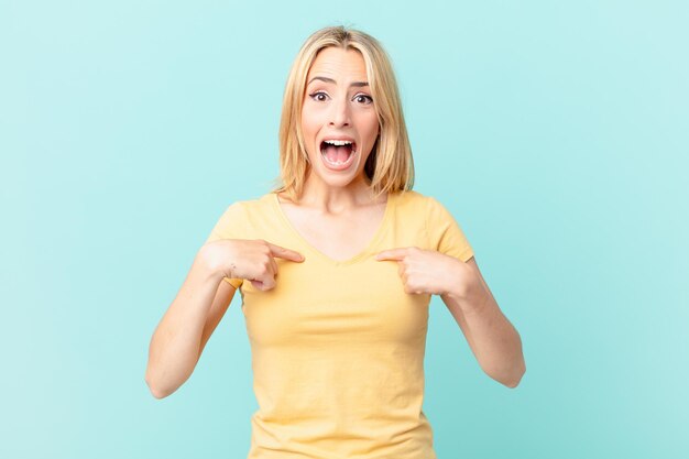 Giovane donna bionda che si sente felice e indica se stessa con un'eccitazione