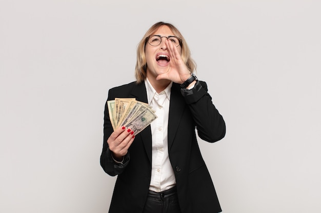 Giovane donna bionda che si sente felice, eccitata e positiva, dando un grande grido con le mani vicino alla bocca, chiamando