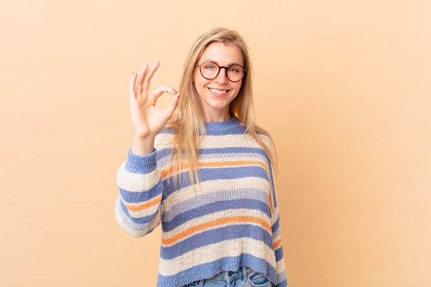 Giovane donna bionda che si sente felice, mostrando approvazione con un gesto ok