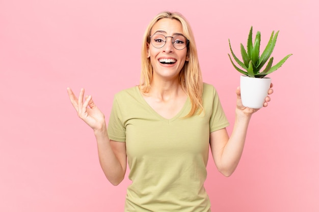 Giovane donna bionda che si sente felice, sorpresa nel realizzare una soluzione o un'idea e tenere in mano un cactus