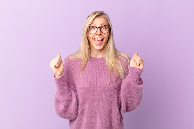 Giovane donna bionda che si sente scioccata, ride e celebra il successo