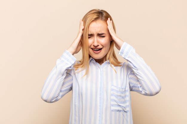 Giovane donna bionda che si sente stressata e ansiosa, depressa e frustrata con un mal di testa, alzando entrambe le mani alla testa