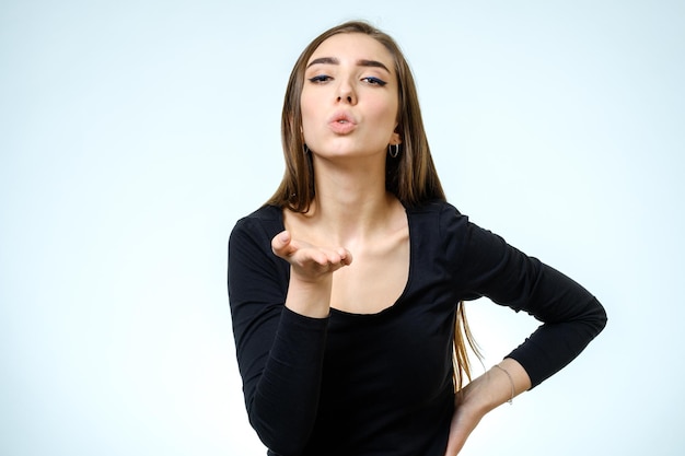 Giovane donna bionda che soffia mentre invia un bacio d'aria alla fotocamera su sfondo bianco