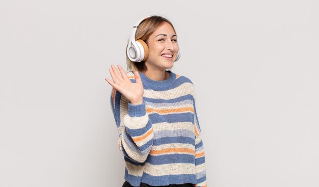 Giovane donna bionda che sorride allegramente e allegramente, agitando la mano, dandoti il benvenuto e salutandoti o salutandoti