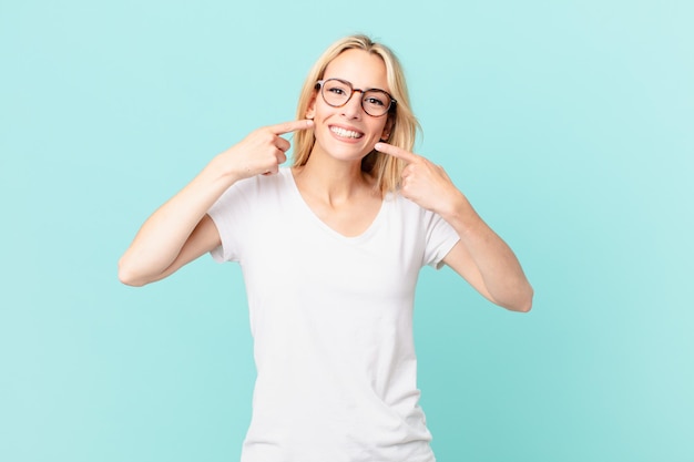 Giovane donna bionda che sorride con sicurezza indicando il proprio ampio sorriso