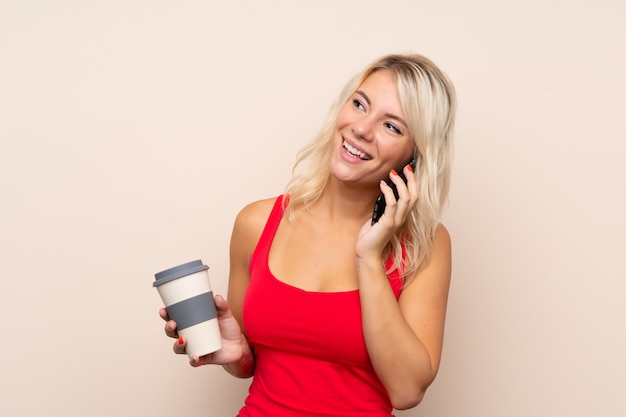 Giovane donna bionda che tiene caffè da portare via e un cellulare