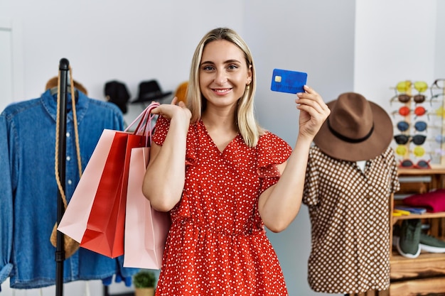 Giovane donna bionda che tiene lo shopping con la carta di credito al negozio di abbigliamento