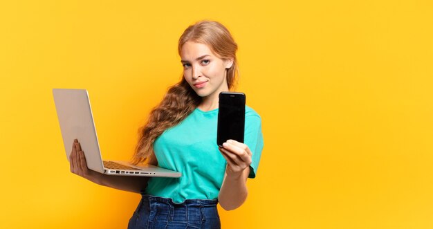 Giovane donna bionda che tiene smartphone e laptop