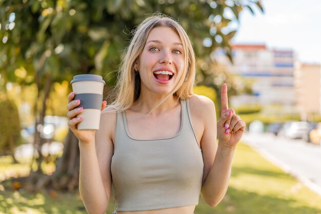 Giovane donna bionda che tiene un caffè da asporto all'aperto indicando una grande idea