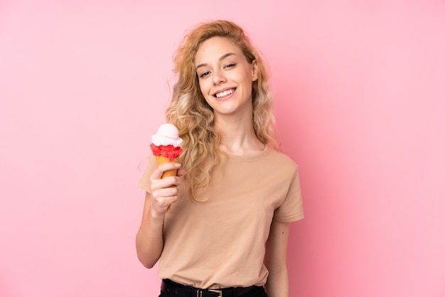 Giovane donna bionda che tiene un gelato della cornetta sul rosa che sorride molto