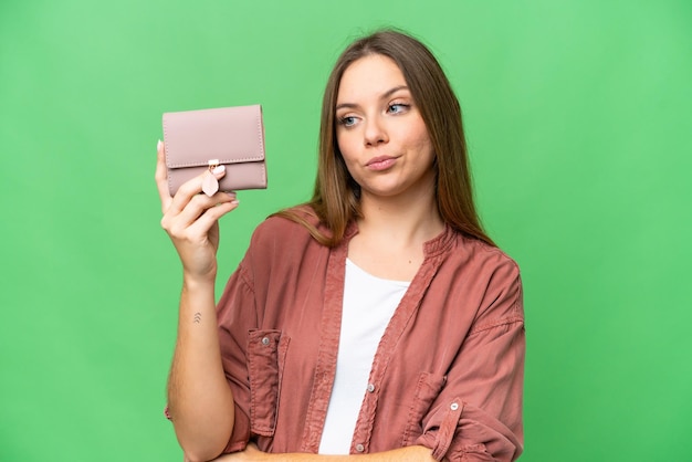 Giovane donna bionda che tiene un portafoglio su sfondo chroma key isolato con espressione triste