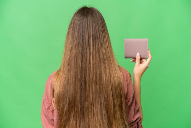 Giovane donna bionda che tiene un portafoglio su sfondo chroma key isolato in posizione posteriore