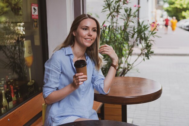 Giovane donna bionda con caffè in un caffè di strada in estate