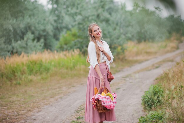 Giovane donna bionda con capelli lunghi in abiti vintage in stile retrò con cestino da picnic a piedi sull'atterraggio