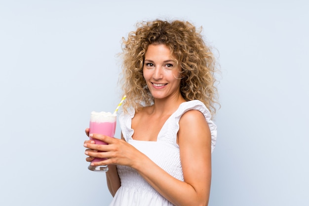 Giovane donna bionda con i capelli ricci in possesso di un frappè alla fragola