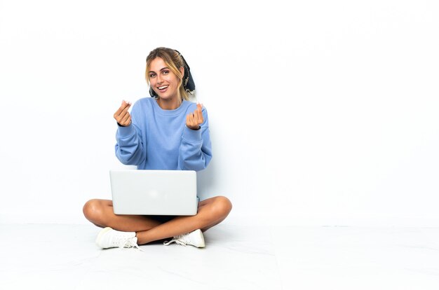 Giovane donna bionda con il computer portatile isolato facendo gesto di denaro