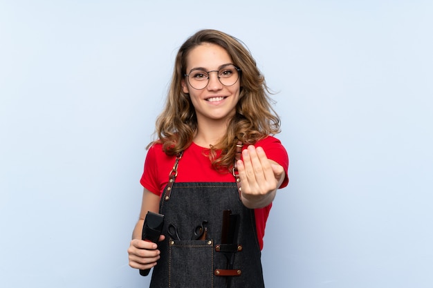 Giovane donna bionda con il grembiule del parrucchiere e la tenuta della tagliatrice dei capelli