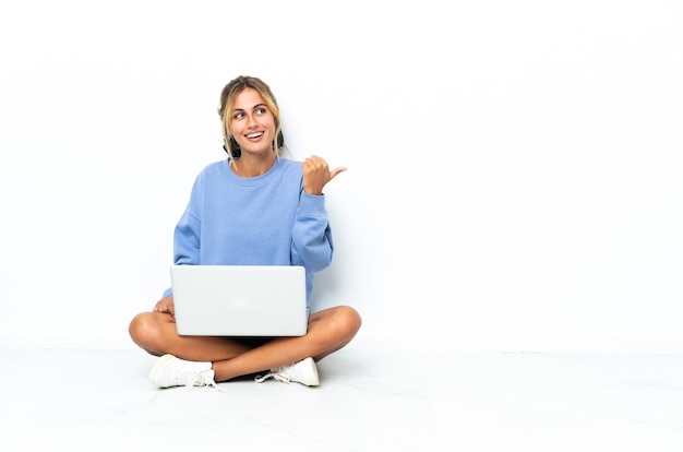 Giovane donna bionda con il laptop isolato che punta al lato per presentare un prodotto