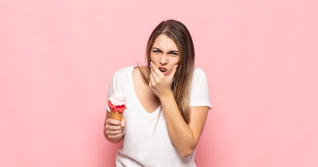 Giovane donna bionda con la bocca e gli occhi spalancati e la mano sul mento, sentendosi spiacevolmente scioccata, dicendo cosa o wow