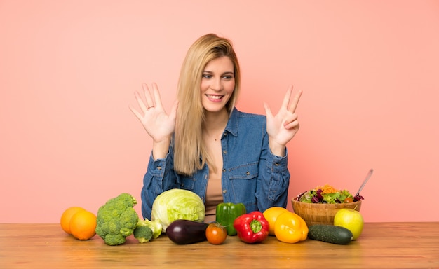 Giovane donna bionda con molte verdure contando otto con le dita