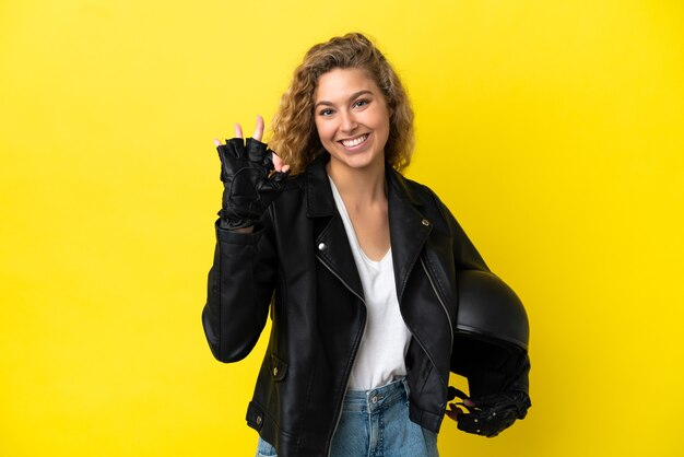 Giovane donna bionda con un casco da motociclista isolato su sfondo giallo che mostra segno ok con le dita