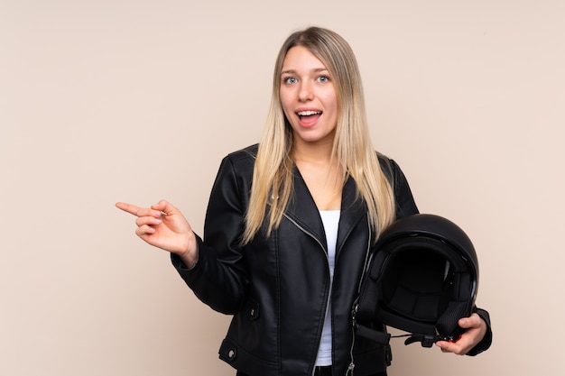 Giovane donna bionda con un casco da motociclista sorpreso e puntando il dito verso il lato