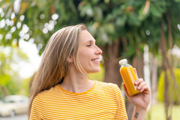 Giovane donna bionda con un succo d'arancia all'aperto