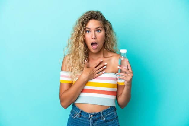 Giovane donna bionda con una bottiglia d'acqua isolata su sfondo blu sorpresa e scioccata mentre guardava a destra