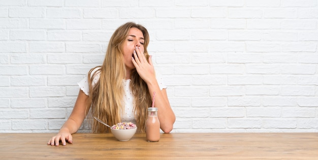 Giovane donna bionda con una ciotola di cereali che copre la bocca