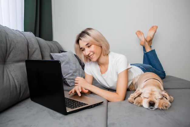 giovane donna bionda con uno spaniel seduto a un laptop blogger che lavora su internet home office