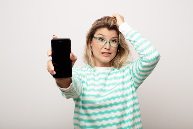 Giovane donna bionda contro la parete piana con uno Smart Phone