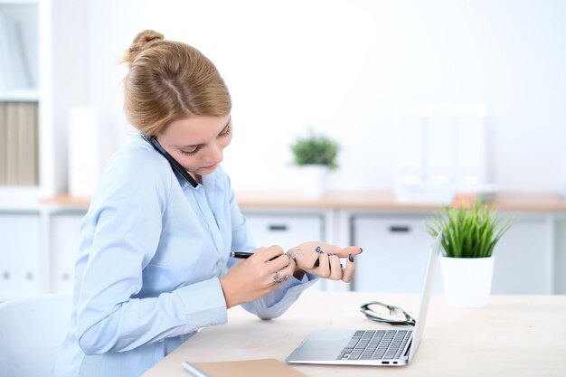 Giovane donna bionda d'affari con il computer portatile in ufficio. Concetto di affari.