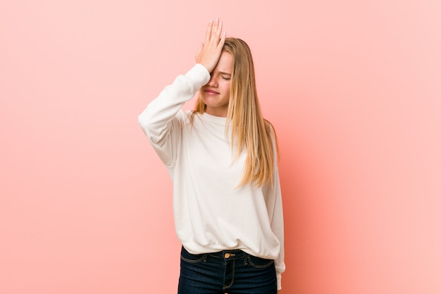 Giovane donna bionda dell'adolescente che dimentica qualcosa, schiaffeggiando la fronte con il palmo e chiudendo gli occhi.