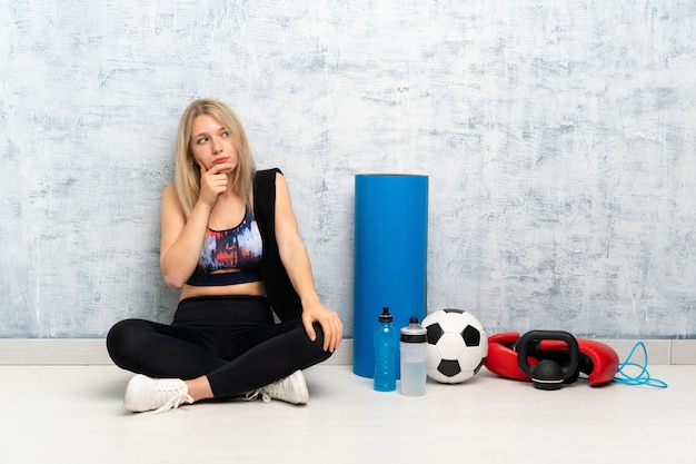 Giovane donna bionda di sport che si siede sul pavimento che pensa un&#39;idea